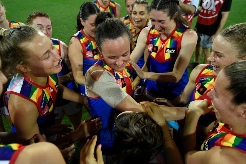 Daisy Pearce is surrounded by her teammates who are all smiling