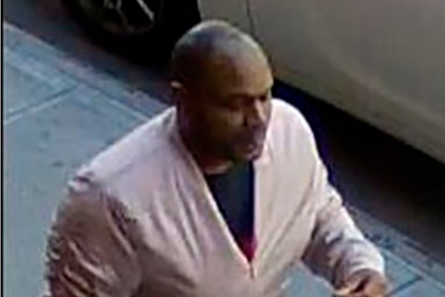 An African-American man in a pink jacket walks along the street, captured by CCTV footage.