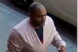An African-American man in a pink jacket walks along the street, captured by CCTV footage.