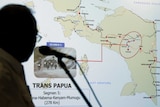 A silhouetted man stands in front of a map of the Papua region.