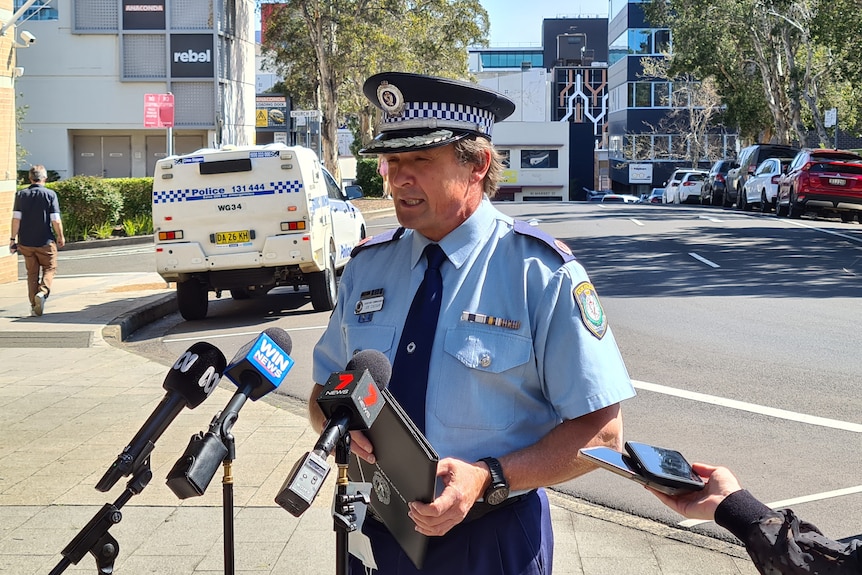 A police officer talking to the media in front of a road.