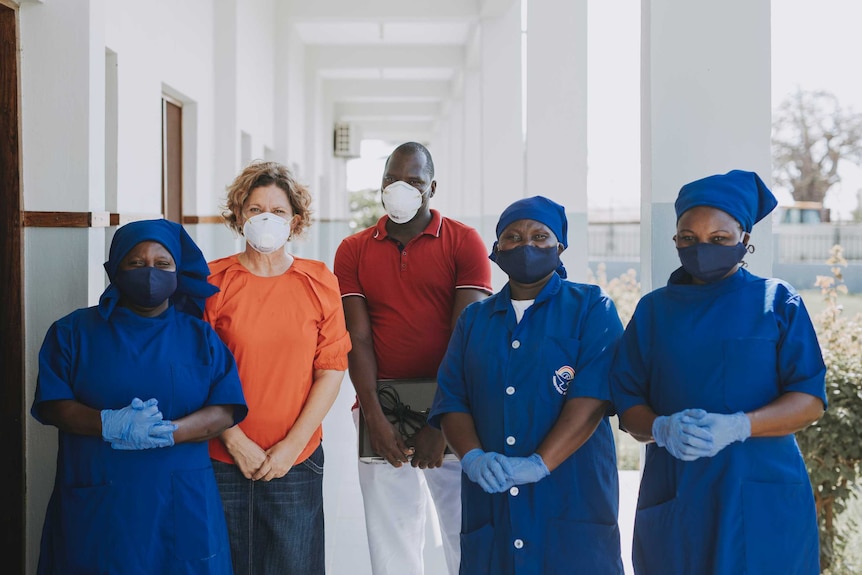 Female and male health workers wearing facemasks while standing in the outdoor corridor of a hospital