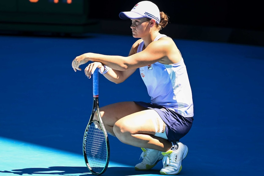 Ash Barty crouches and leans on her racquet during a break in her Australian Open match against Karolína Muchová.
