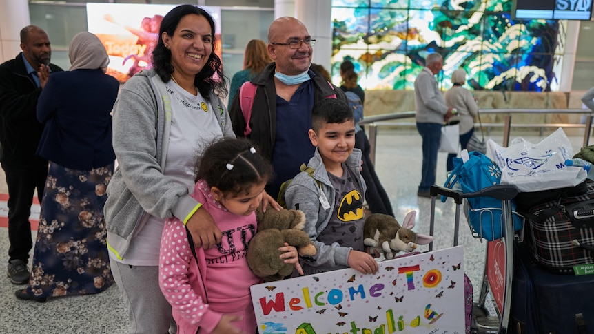 a family made up of a woman, a man, a young girl and young boy stand and smile at the airport