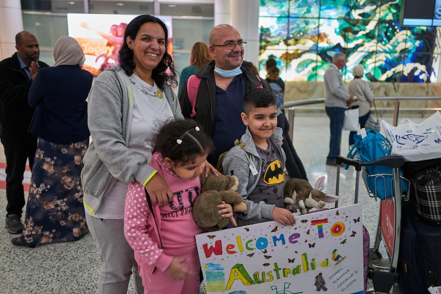 a family made up of a woman, a man, a young girl and young boy stand and smile at the airport