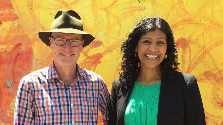 Tim Read smiles in a felt hat and checked shirt, next to Samantha Ratnam in a black jacket.