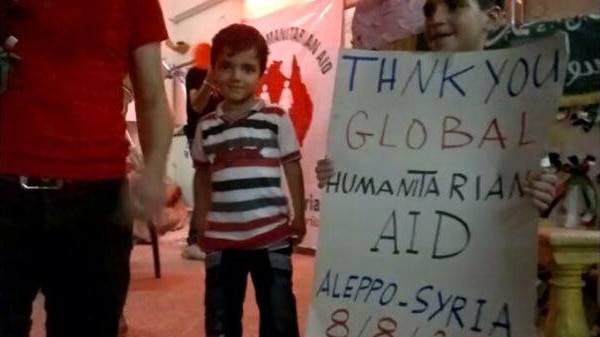 Child smiles holding a sign with English text written on it as another smaller child smiles