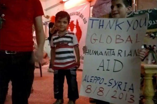 Child smiles holding a sign with English text written on it as another smaller child smiles