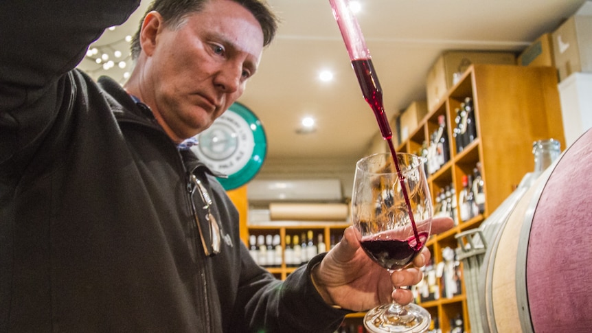 Tony Harper uses a tool to pour wine into a glass.