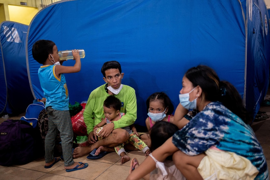 Young family of six sit in front of a tent inside an evacuation centre ahead of Typhoon Noru.