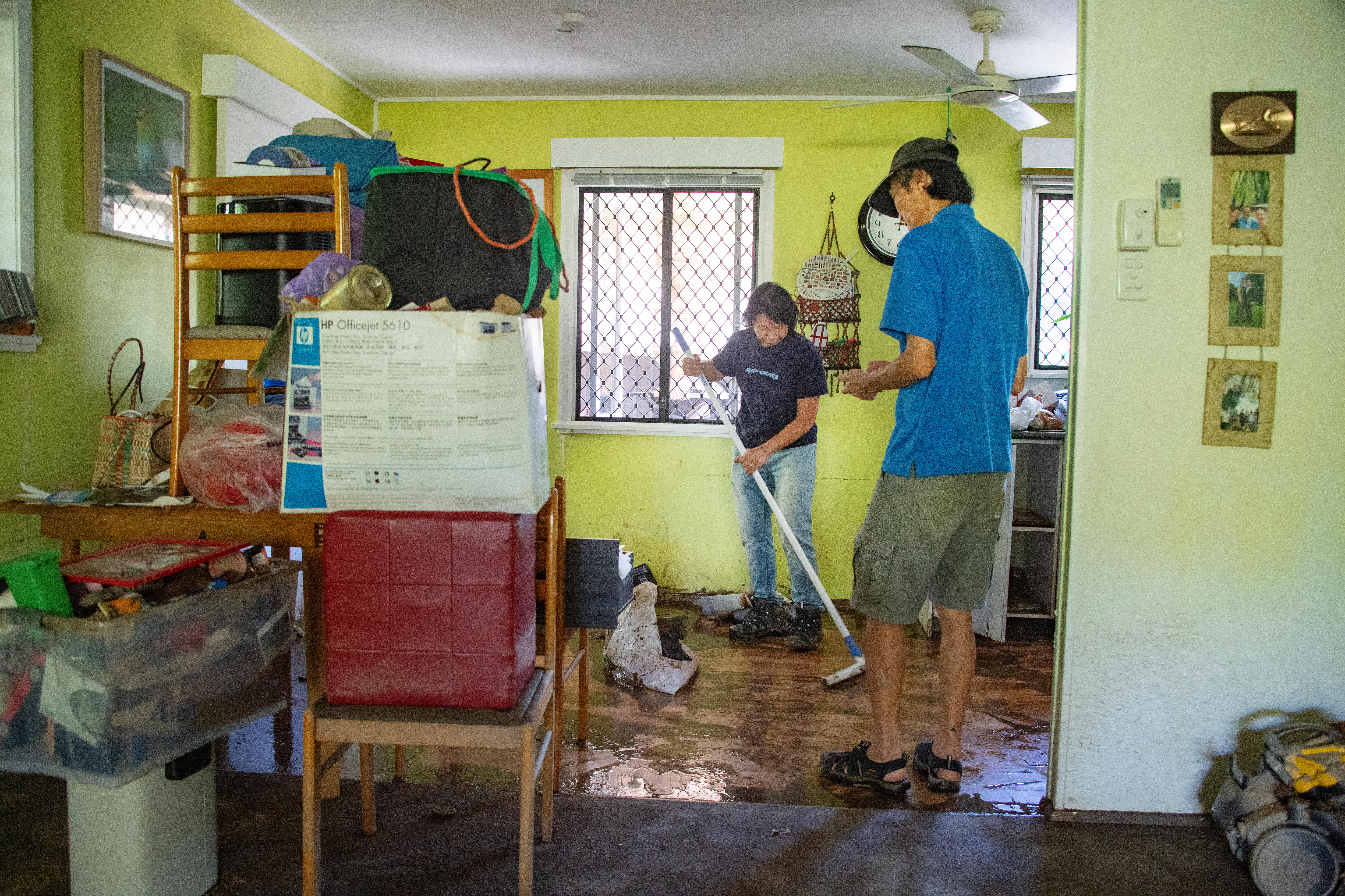 a man and woman sweeping the mud from their flooded home