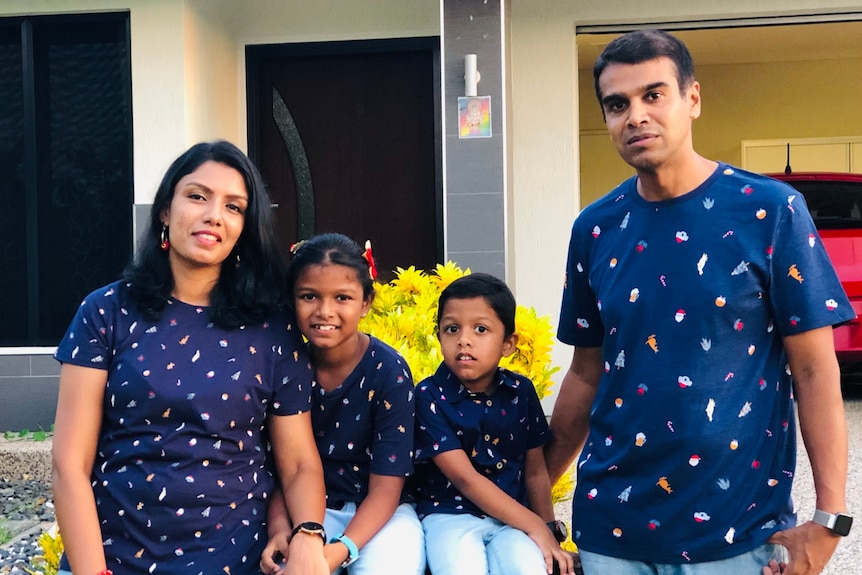 A family of four poses for a photo with matching shirts. 