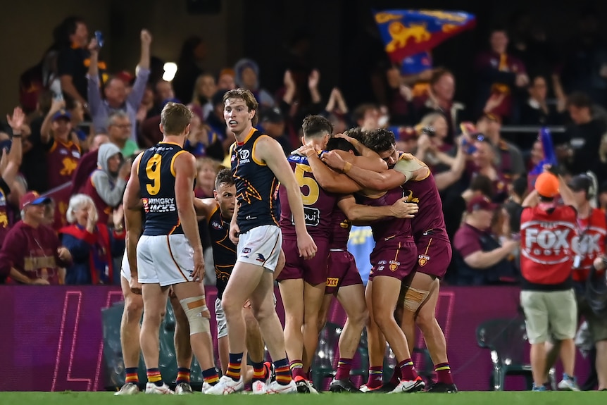 Two Adelaide Crows players look dejected afte a match while in the background Brisbane Lions players celebrate.