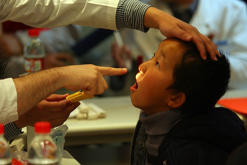 A young Chinese boy having his mouth and lips inspected with a light by a doctor, in Nanjing China