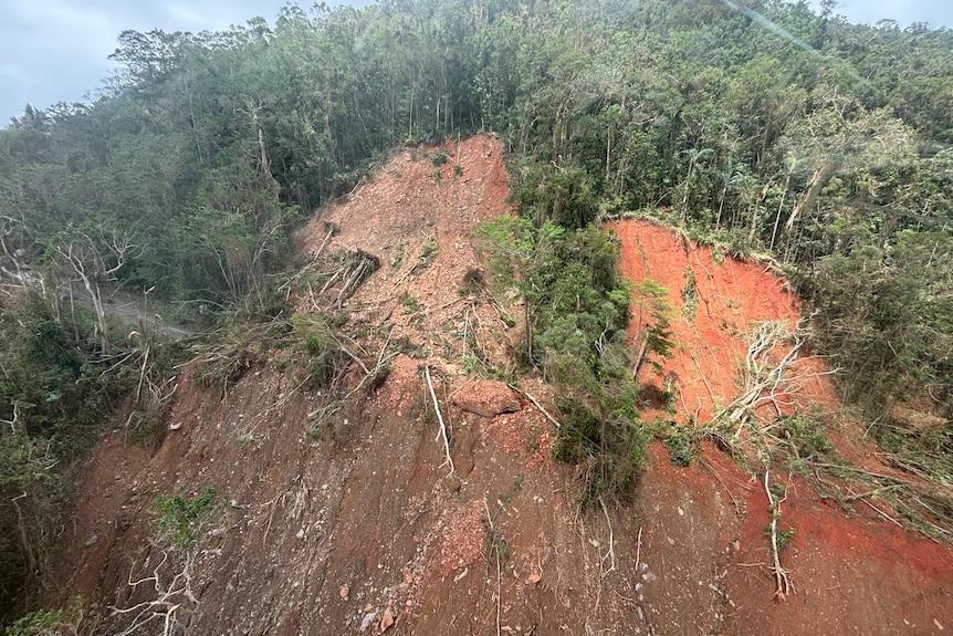 A major landslide with dirt, trees and rocks covers the road
