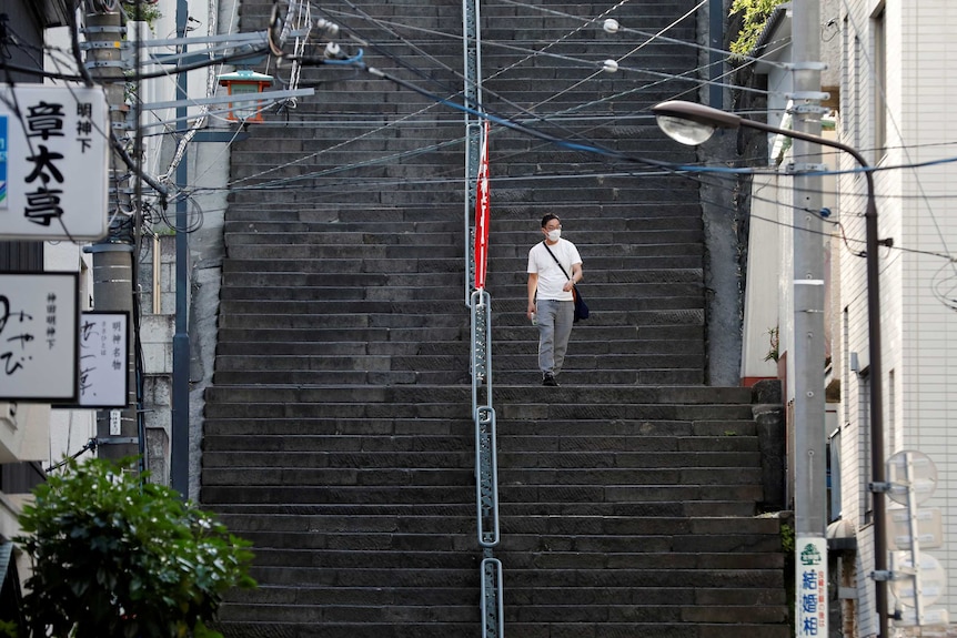A man wearing a protective face mask walks down stairs with nobody else around.