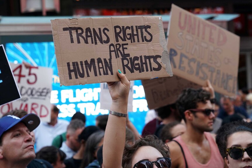 A woman holds up a sign saying "trans rights are human rights" at a public protest.