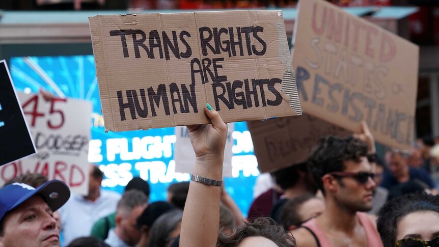 A woman holds up a sign saying "trans rights are human rights" at a public protest.
