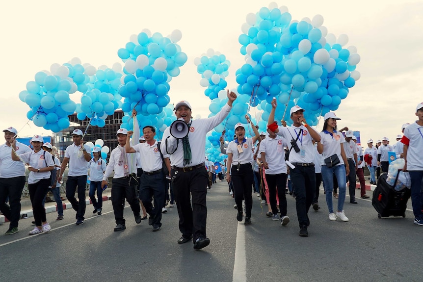 A man with a megaphone leads a rally in front of people carrying balloons