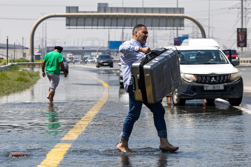 A man carries a suitcase through floodwater.