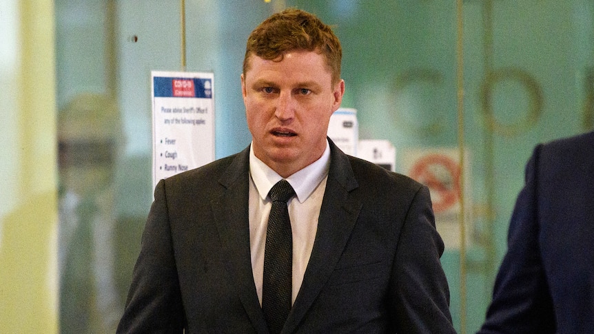 a man looking at the camera walking out of a court room