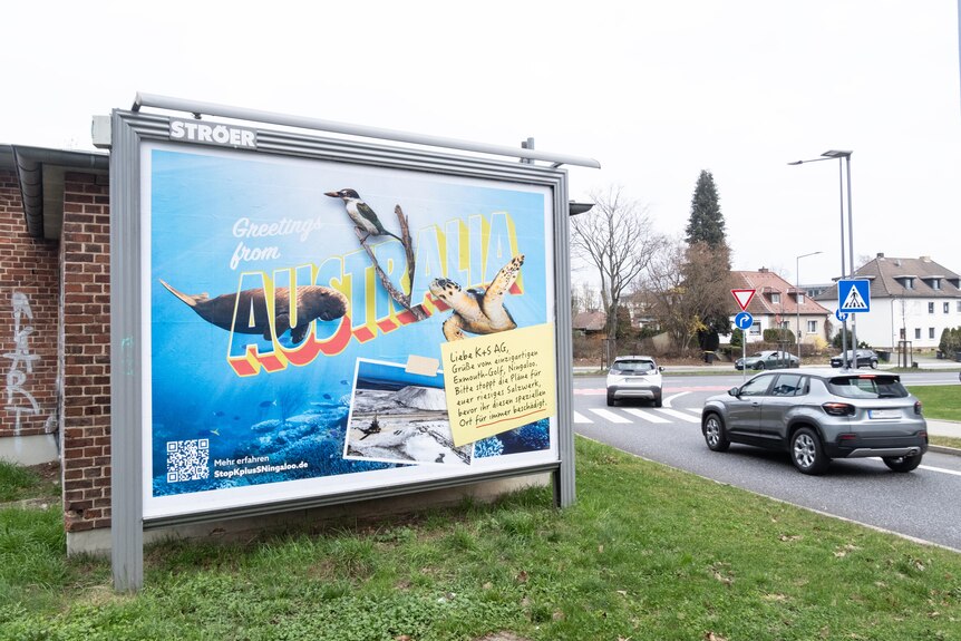 A bright postcard-style billboard by the road features a sea turtle, bird, and dugong alongside a photo of a salt mound.