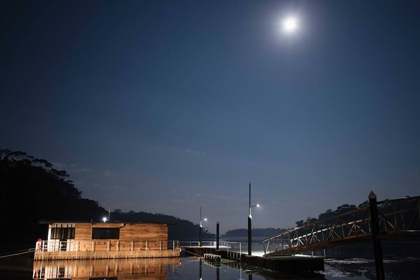 A houseboat on a lake with a full moon lighting the night sky