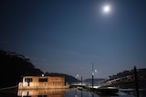 A houseboat on a lake with a full moon lighting the night sky