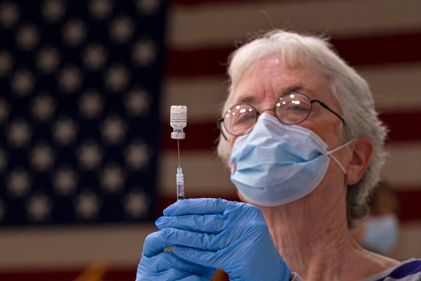 A woman fills a syringe with COVID-19 vaccine at a clinic.