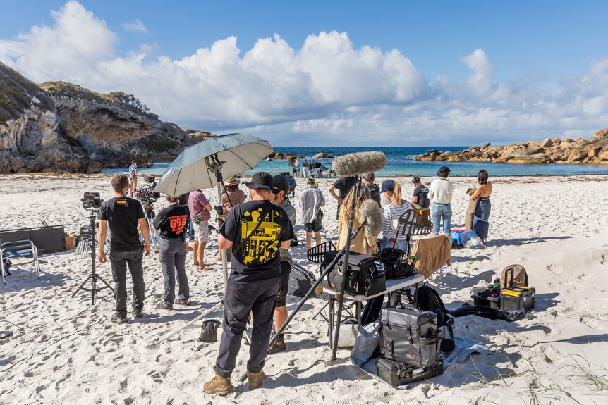 crew standing around with microphones filimg on beach