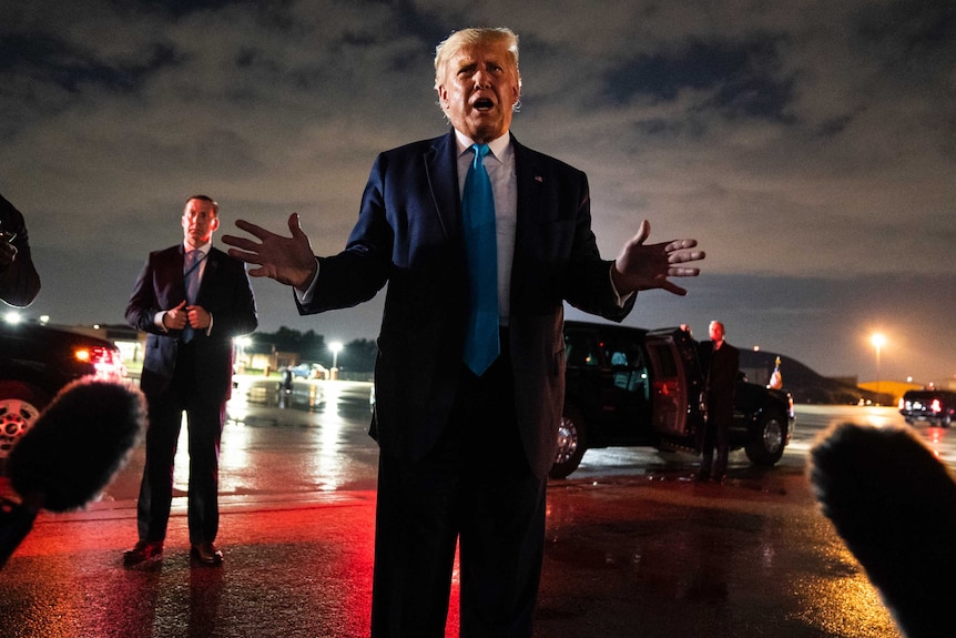 President Donald Trump talks with reporters as he stands on a airfield runway at night.