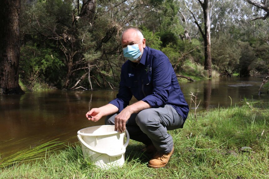 A man crouching with a bucket near a river.