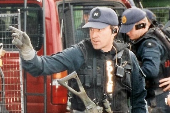 A man wearing an armoured vest has a large gun strapped across his chest.