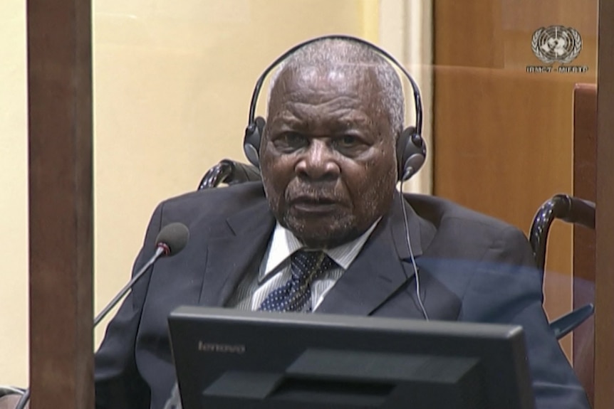 Felicien Kabuga wears headphones and a suit as he sits in a wheelchair at a hearing.