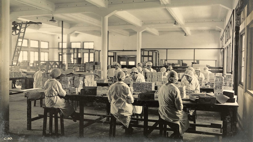 Sepia photo of a factory floor with women in white coats and hairnets wrapping chocolate