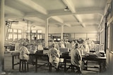 Sepia photo of a factory floor with women in white coats and hairnets wrapping chocolate