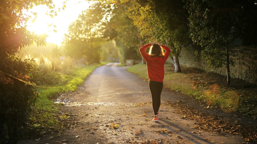 A woman walks a country road with the sun rising ahead of her