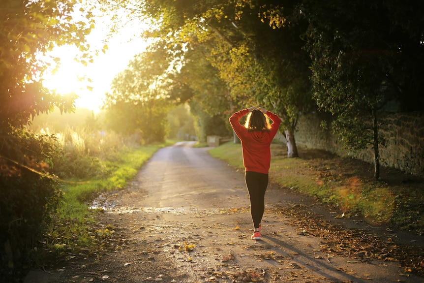 A woman walks a country road with the sun rising ahead of her