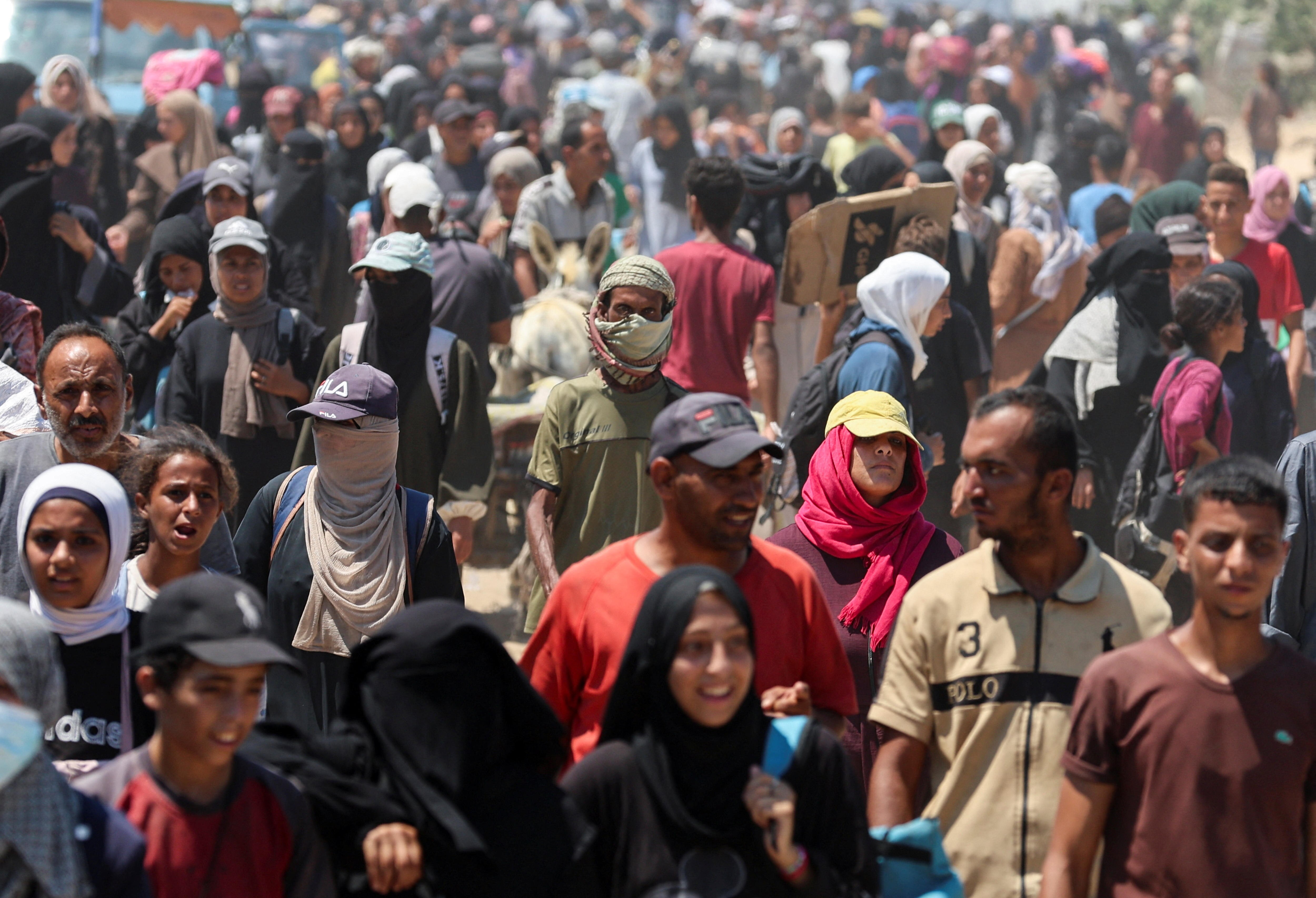 A large and dense crowd of Palestinians, some carrying sacks and boxes, walk along a road.