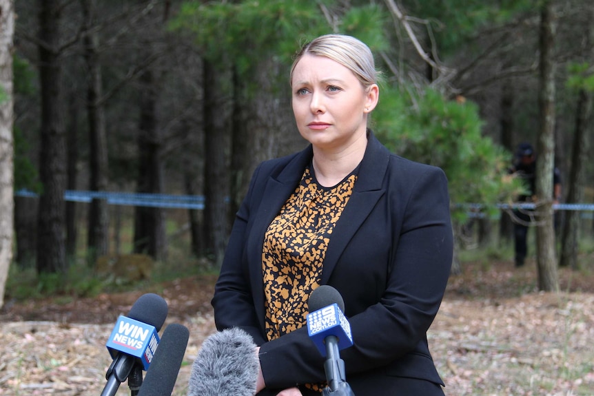 A woman stands in a forest surrounded by microphones.