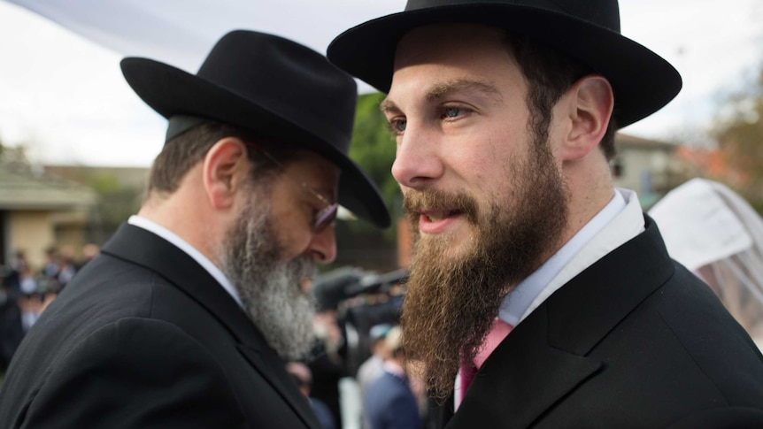 A young Jewish man, flanked by an older one, each in identical beard and black hat.