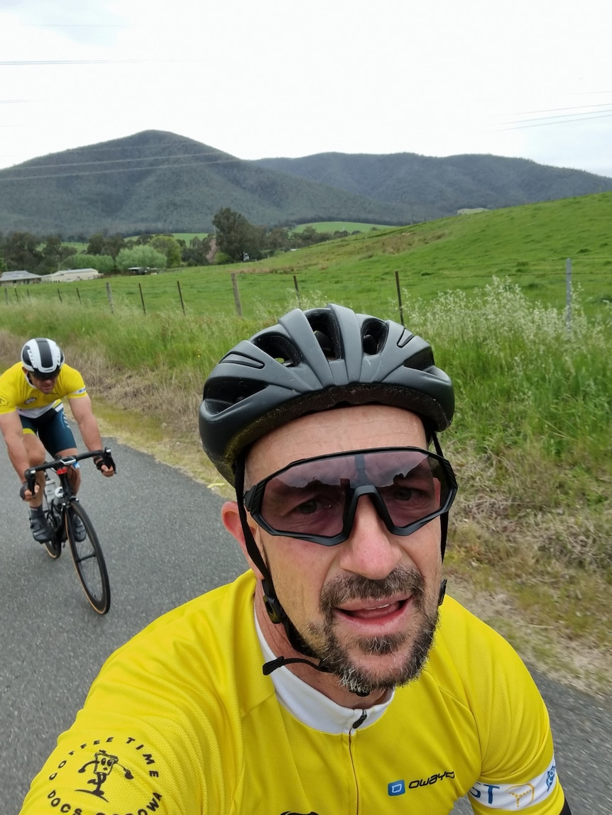 Two men on bikes with hills in the background.