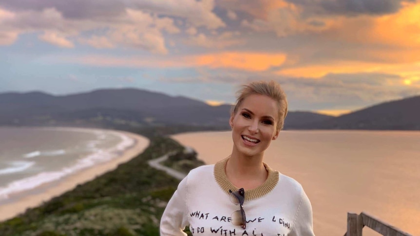 Doctor of neuroscience smiling with a sunset over Bruny Island behind her