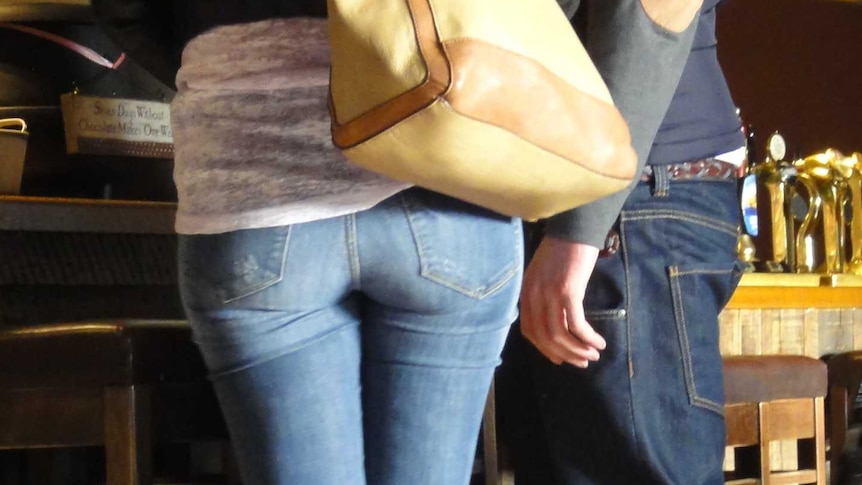 photograph of a woman and a man standing at a bar with man's hand close to woman's bottom