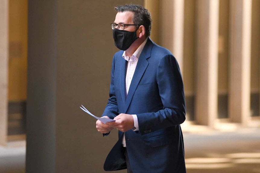 Victorian Premier Daniel Andrews in a black face mask, carrying notes.