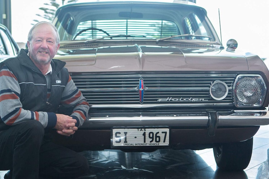 A man squating in front of restored HR Holden car