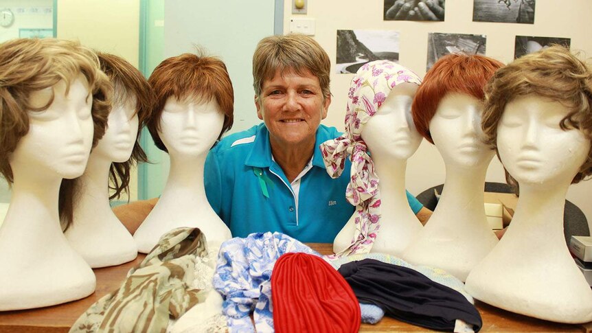 Ellen Traeger in the middle of six manequin heads with wigs.