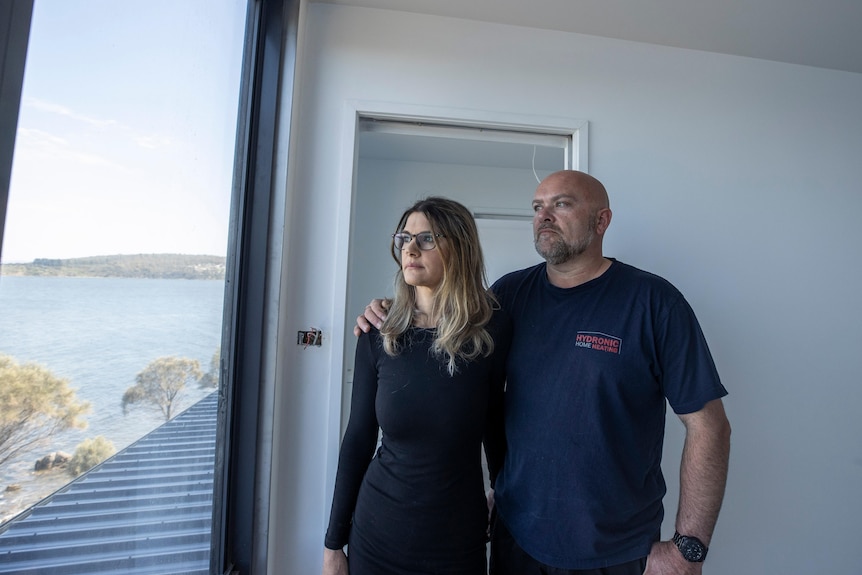 A couple look out a window in an unfinished house.