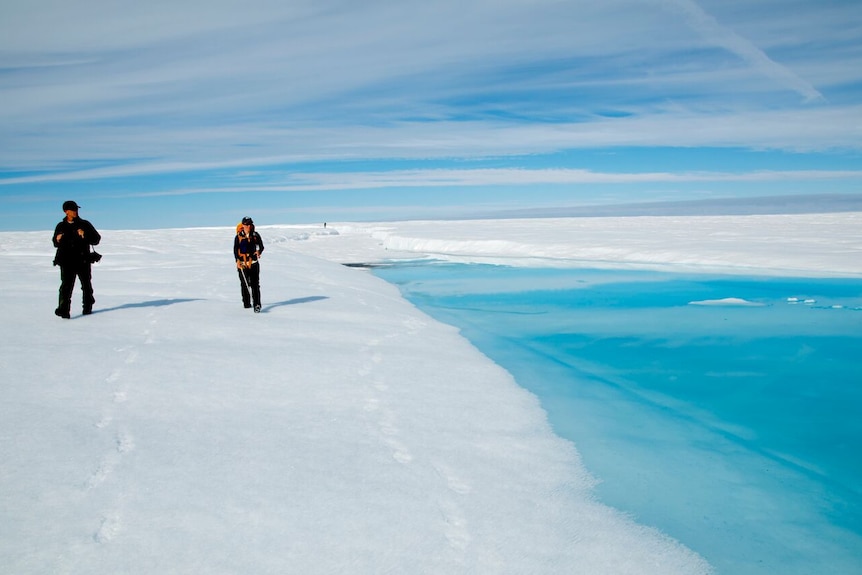 Two scientists walk beside a glacial lake in Greenland.