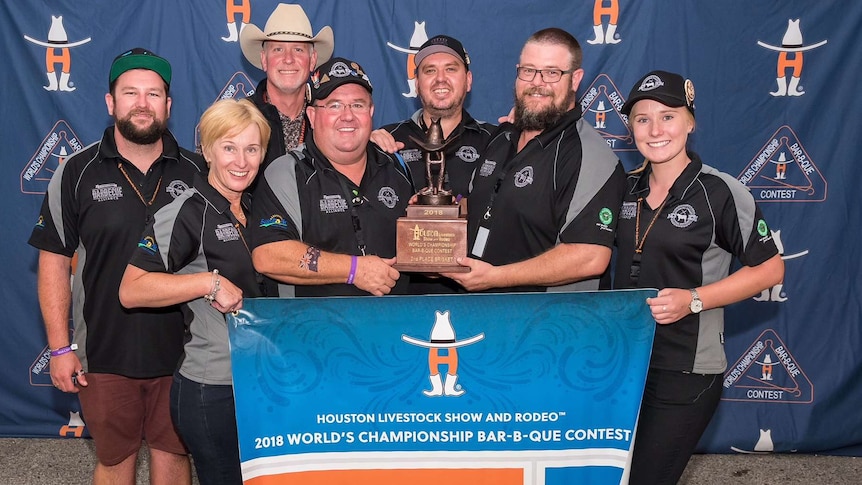 Group of people, some wearing hats, hold a trophy